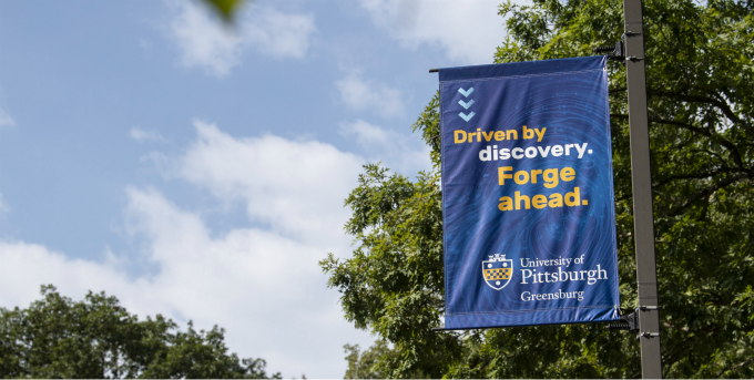 Blue & gold campus banner reading Driven by discovery. Forge ahead.