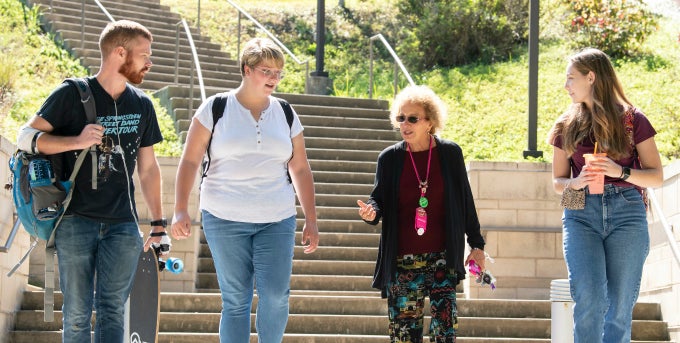 Three students walking on campus with faculty member