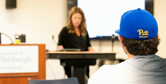 Photo of student facing instructor. The back of the student's hat has the Pitt-Greensburg script logo on it.