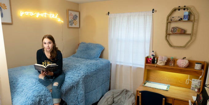 Student sitting on bed reading in residence hall room