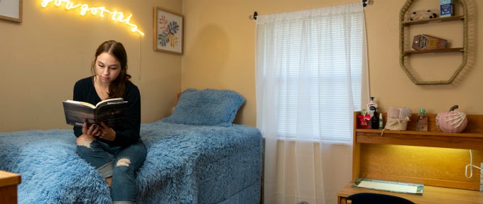 Student seated on bed reading in Westmoreland Hall bedroom