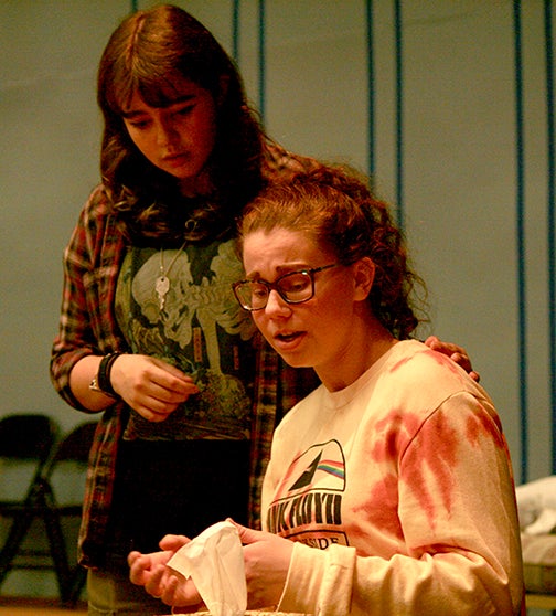 Student actor standing next to seated student actor.