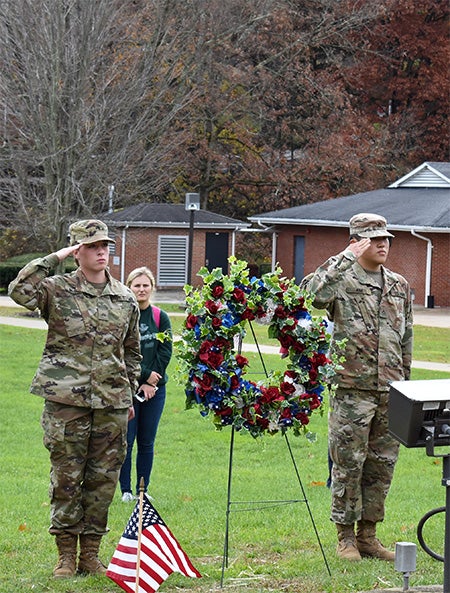 Two servicepeople saluting near patriotic wreath