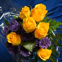 Six (6) yellow roses and blue flowers with greens, wrapped in cellophane, and tied with a ribbon.  $25.50 each