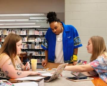 Student standing, speaking to two seated students.
