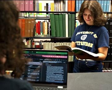 A student looks inside a book while at the campus library.