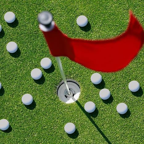 Golf balls scatterd on the green around a golf hole and flag.